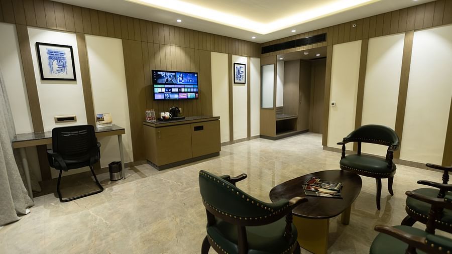 A comfortable seating area with chairs and a coffee table facing a TV and desk at Pride Resort, Jodhpur, under soft lighting.