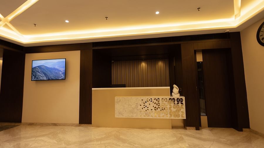 A sleek reception desk with decorative panel and a wall-mounted TV in a well-lit lobby at Pride Resort, Jodhpur.
