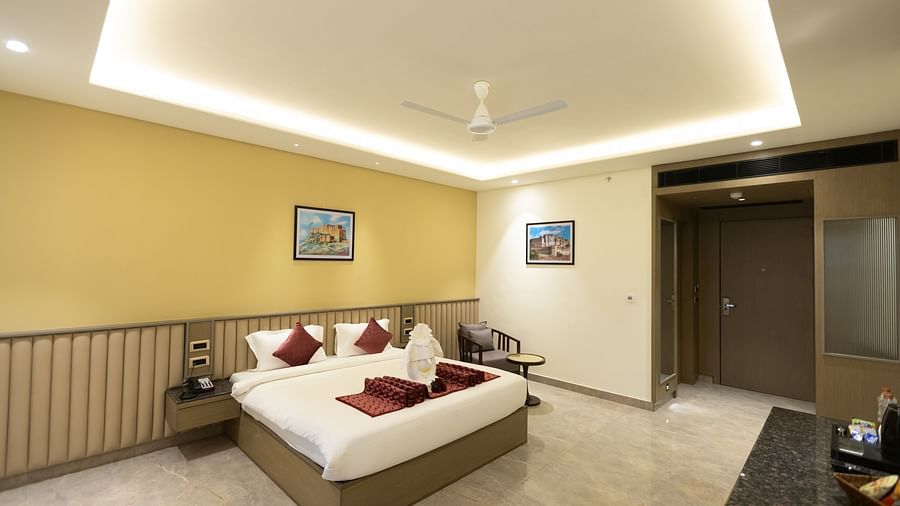 A spacious hotel room at Pride Resort, Jodhpur, featuring a large bed with cushions and towel art under soft ceiling lighting.