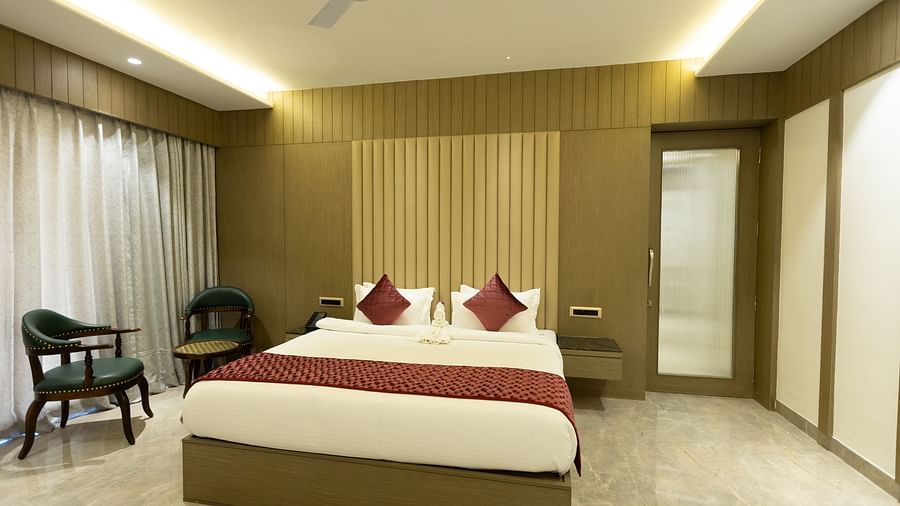 A bright hotel room at Pride Resort, Jodhpur, with a large bed, two chairs by the window, and built-in wardrobes.