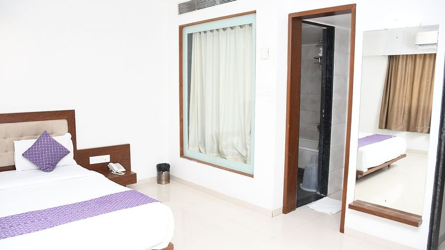 View of the Paradise VIP Suite at Pushpak Resort, Shirdi, showcasing a cozy bed, a wall-mounted mirror, and an entrance to the washroom