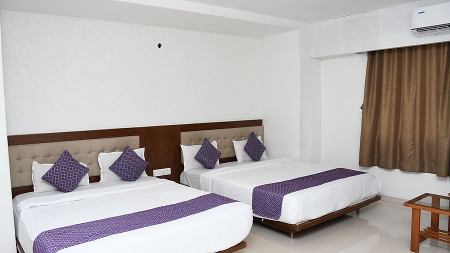 Premium Family Club Room at Pushpak Resort, Shirdi, featuring separate beds, a wall-mounted AC, and a small table