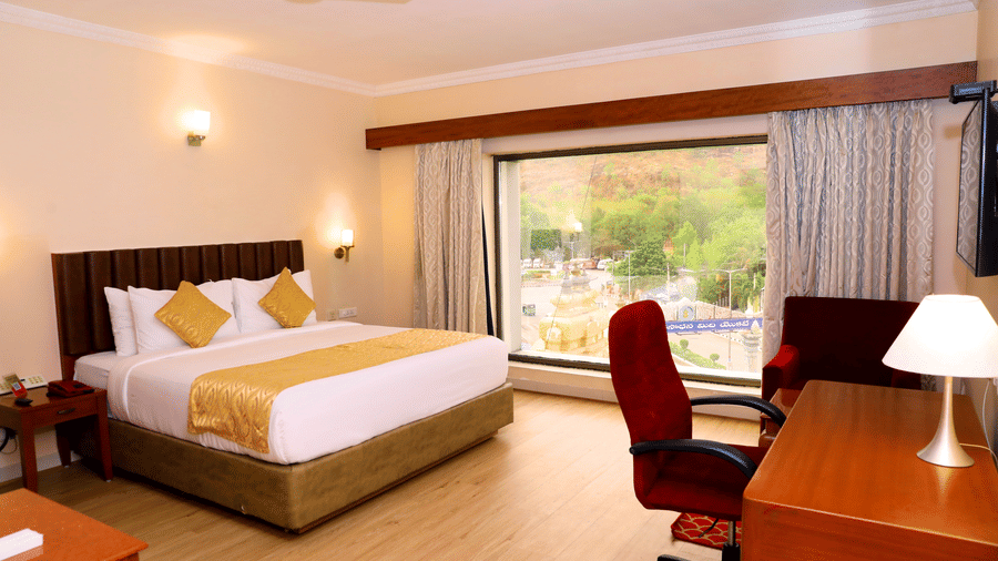 Hill View Room featuring a floor to ceiling window, a double bed, and desk and a chair inside Raj Park, one of the top hotels in Tirupati