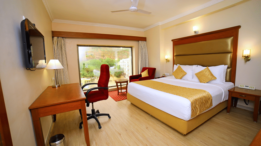 Hill View Room featuring a double bed facing a TV with a lamp on the work desk below, and a sofa next to the window at Raj Park Hotel, offering the best place to stay in Tirupati