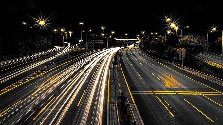 an image taken with long exposure showing vehicles' headlights as a trail in the highway during the night