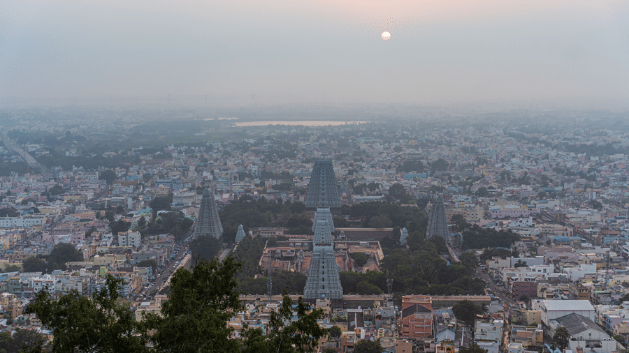 An aerial view of the town of tirupati with numerous temple's gopuram in view and other buildings and trees also in view with the sun setting in the background.