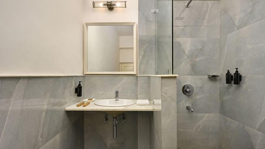 A bathroom at Ram Pratap Palace, Udaipur, with marble-patterned tiles, a white sink, a large mirror, and a modern glass-enclosed shower area.
