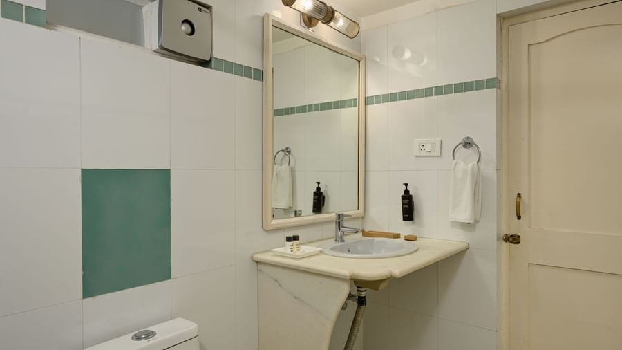 A well-lit bathroom at Ram Pratap Palace, Udaipur, with white tiled walls, a marble sink counter, a large mirror, and a wall-mounted toilet.