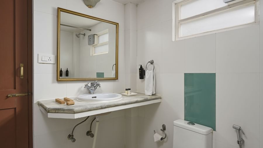 A minimalist bathroom at Ram Pratap Palace, Udaipur, with white tiled walls, a marble counter with a sink, and a gold-framed mirror.