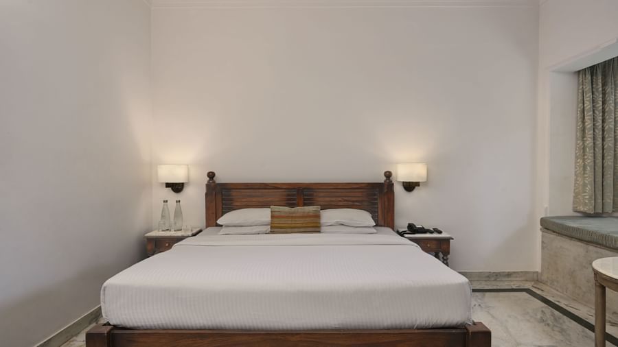 A well-appointed room at Ram Pratap Palace, Udaipur, featuring a large wooden bed, two side tables with lamps, and a window seat.