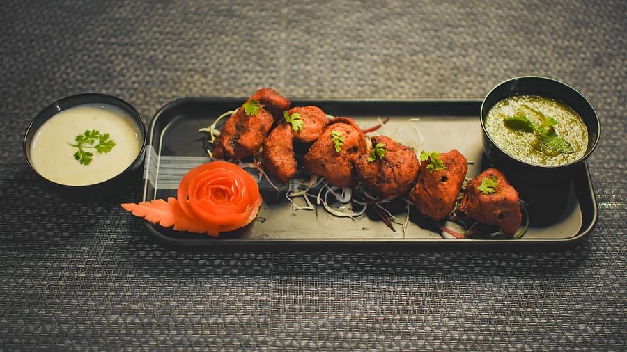 A chicken kebab on a rectangular plate, with sauce on the side and a small bowl of sauce beside it
