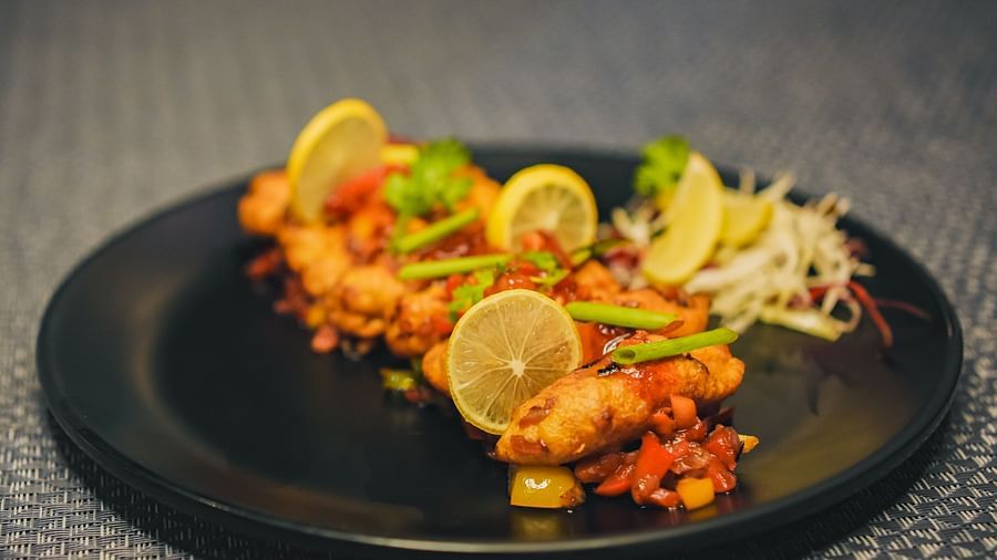 A plate of fried pakoda topped with veggies and sauce, accompanied by a side of salad and lemon