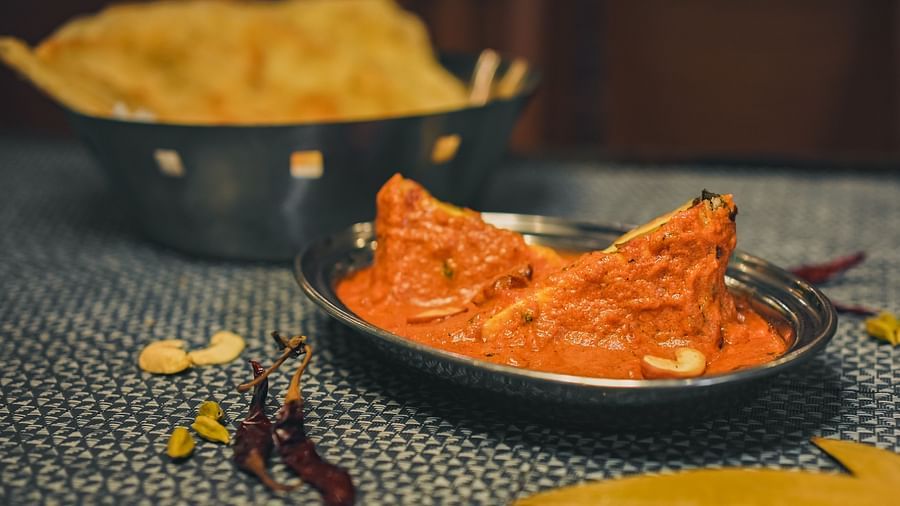 A serving of curry on a steel plate, accompanied by roti on another plate, with various spices put on the table