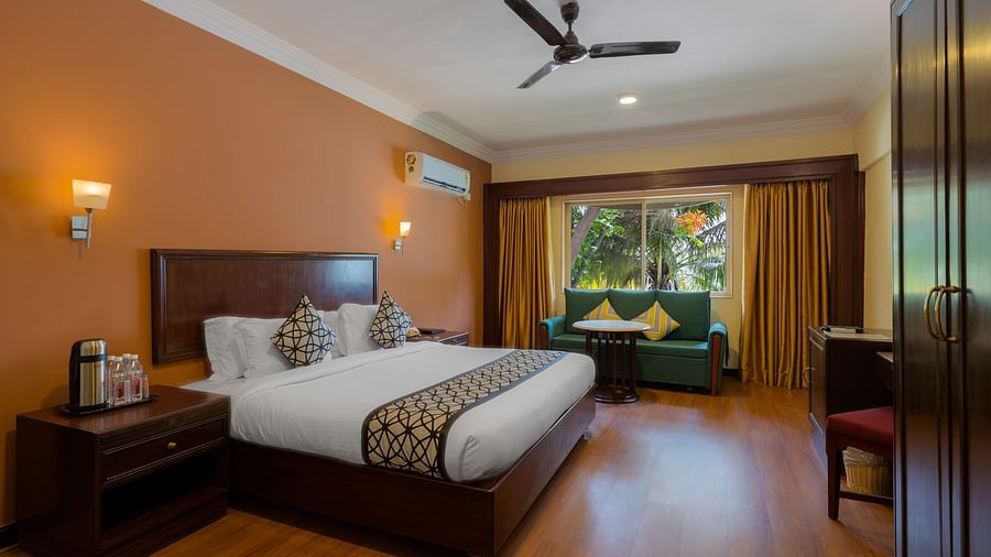An image of a bedroom with king size bed with bedside tables, lamps, cabinets. and an open window - Ras by Treat Resorts