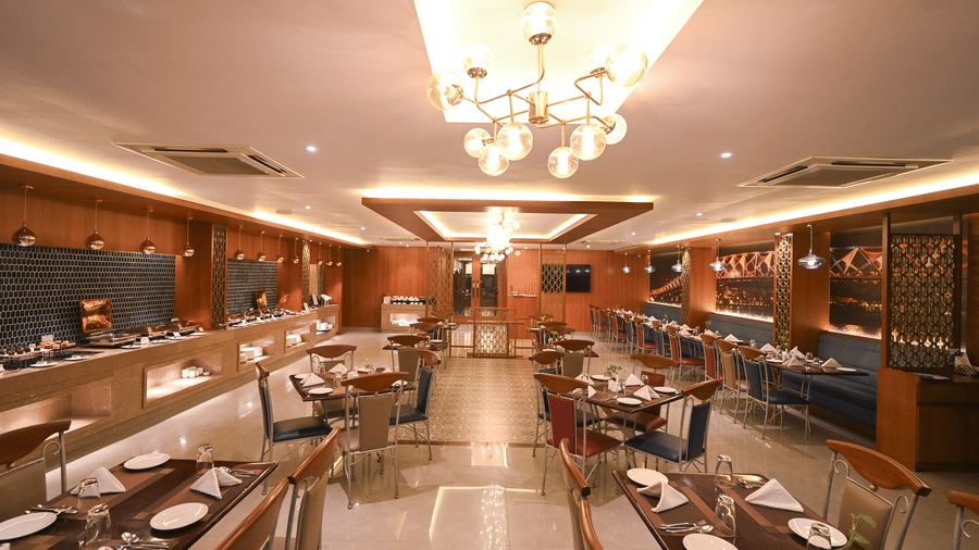 Elegant restaurant dining hall at Rivera Sarovar Portico, Ahmedabad featuring neatly arranged dining tables, decorative chandeliers and contemporary interiors.