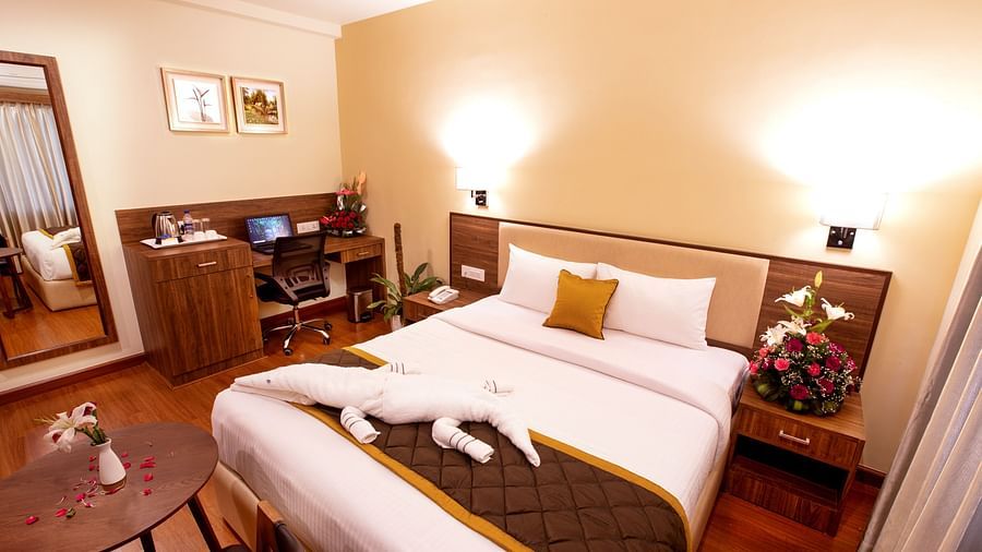 A warm and inviting hotel room with a plush bed, wooden furnishings, a work desk, and soft lighting for a cosy ambiance. - RK Gardenia, Surya City