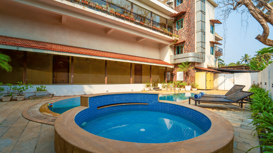 Rosetum Anjuna's circular children's pool with blue mosaic tiles in the foreground, the main swimming pool behind, sun loungers with towels, and the hotel facade in the background.