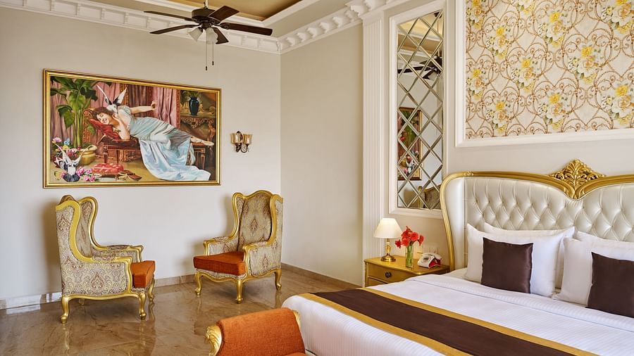 armchairs below a painting and a double bed in the PREMIER ROOM - Royal Kingdom Sarovar Portico, Pilibhit