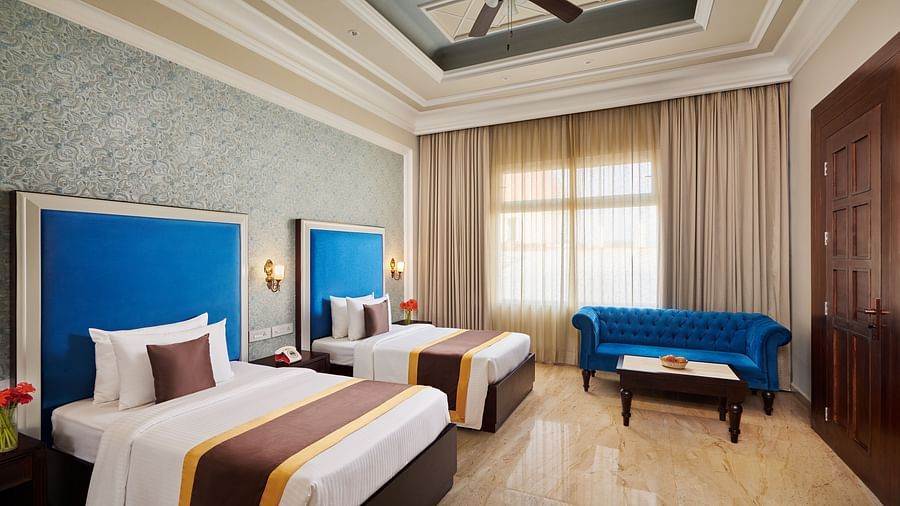 twin beds and a blue sofa next to a coffee table in the PREMIER ROOM - Royal Kingdom Sarovar Portico, Pilibhit