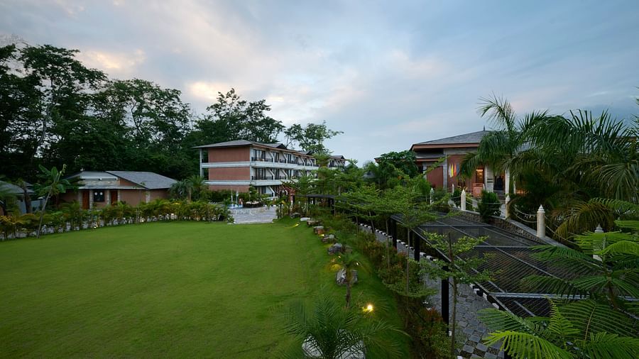 A spacious green lawn in front of the hotel with trees lining the property - Royal Tulip, Chitwan