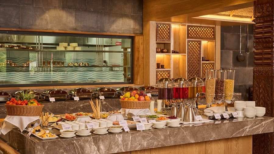 Well-lit buffet counter with an array of breakfast options and a wooden ceiling - Royal Tulip, Chitwan