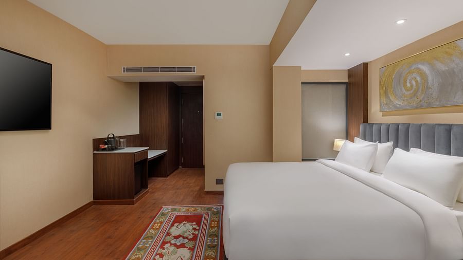 A comfortable bedroom at Royal Tulip, Kathmandu, featuring a plush bed, flat-screen TV, and work desk.