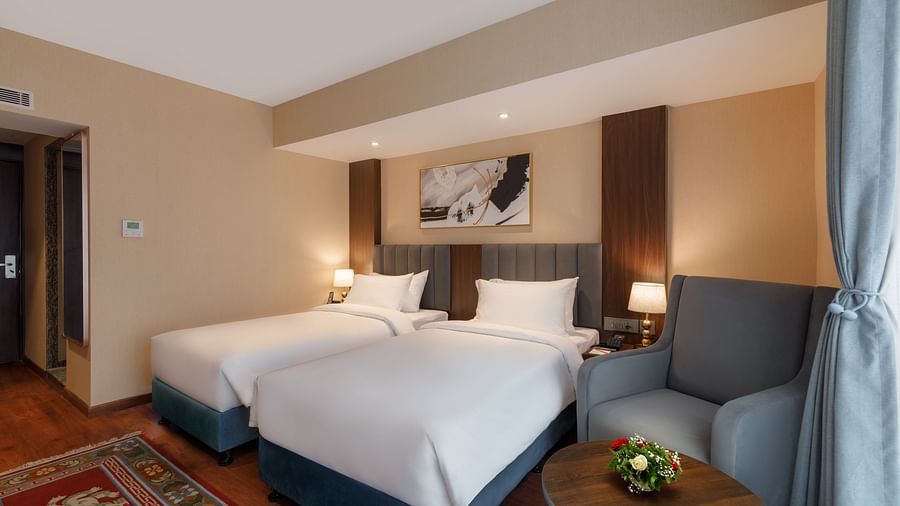 Twin beds in a well-appointed room at Royal Tulip, Kathmandu, with a comfortable armchair and side table.