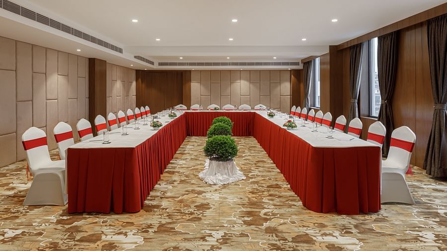 A U-shaped meeting room at Royal Tulip, Kathmandu, with a central floral arrangement and red-accented chairs.