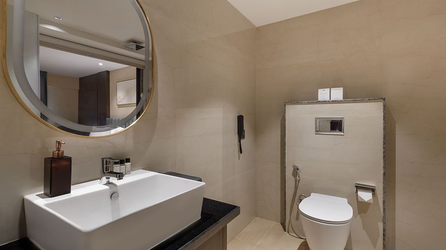 Modern bathroom at Royal Tulip, Kathmandu, featuring a sleek white basin, round mirror, and toilet.