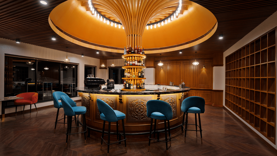 A circular bar at Royal Tulip Shivapuri National Park - Kathmandu with stools and a unique golden light fixture hanging from the ceiling.