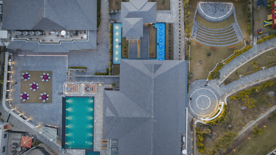 Bird's-eye view of Royal Tulip Shivapuri National Park - Kathmandu showing the swimming pool, rooftops, stone walkways, and outdoor courtyard.