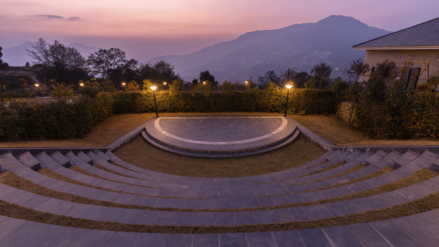 An outdoor stone amphitheater with tiered seating overlooking a valley at Royal Tulip Shivapuri National Park - Kathmandu during twilight.