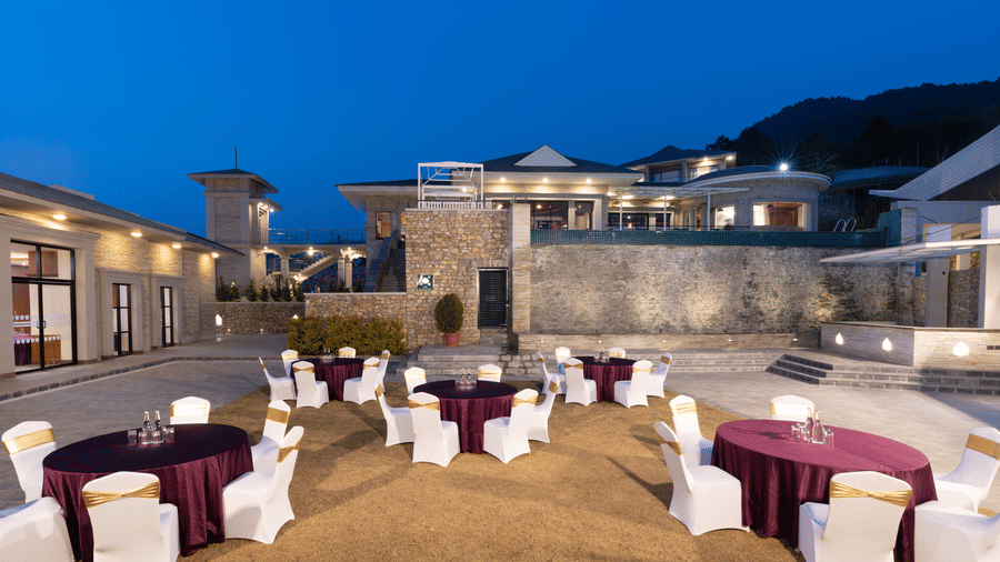 Outdoor event space at Royal Tulip Shivapuri National Park - Kathmandu set with round tables, purple cloths, and chairs under a dusk sky.
