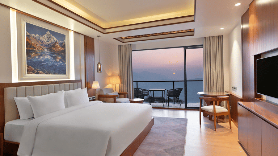 An Executive Room at Royal Tulip Shivapuri National Park - Kathmandu featuring a white king bed, mountain artwork, and a balcony with a sunset view.
