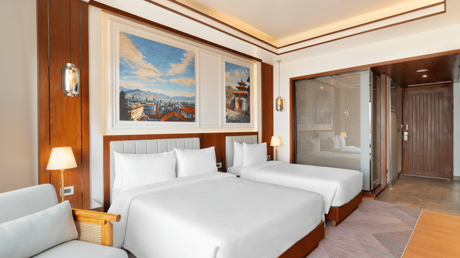 A spacious Executive Room bedroom at Royal Tulip Shivapuri National Park - Kathmandu with twin beds, wood accents, wall lamps, and a view into a hallway.
