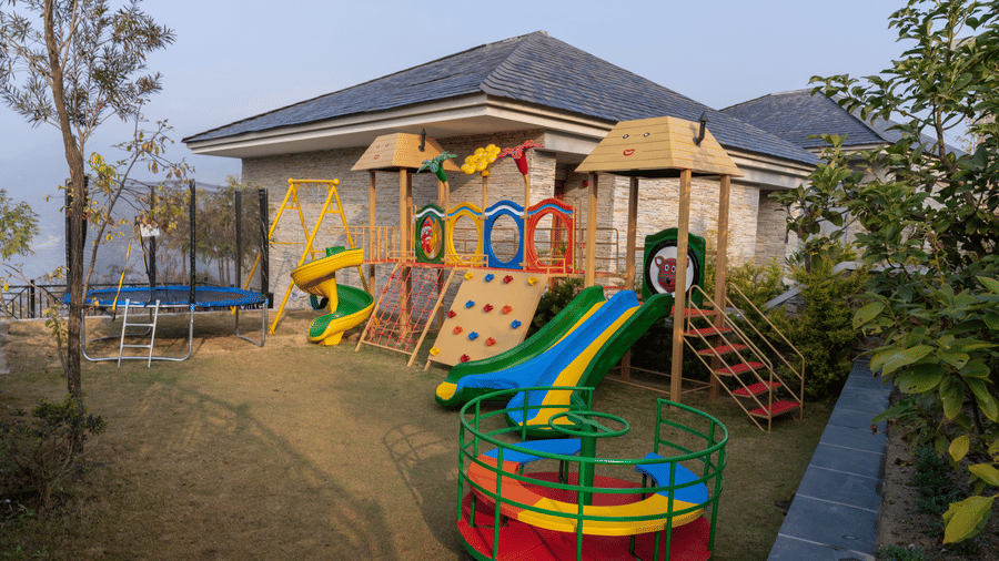 Outdoor colourful playground with slides and a climbing wall at Royal Tulip Shivapuri National Park - Kathmandu, located next to a building.