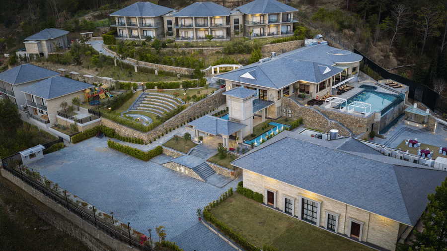 High-angle view of the Royal Tulip Shivapuri National Park - Kathmandu resort complex, showing multi-story buildings, a pool, and tiered stone landscaping.