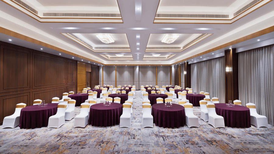 Indoor ballroom at Royal Tulip Shivapuri National Park - Kathmandu featuring round tables with linens and rows of white chairs.
