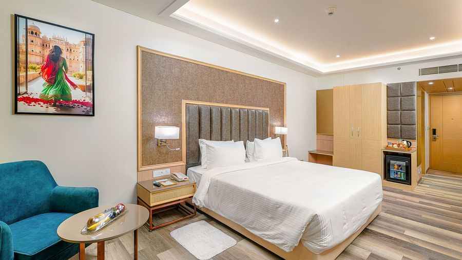 Junior Suite with king bed, accent chair, and wall art at Sarovar Portico, Ajmer.