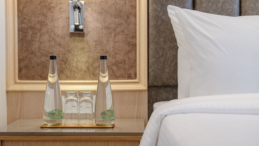 A close up shot of a night stand with bottled water and a bed to its right - Sarovar Portico, Ajmer