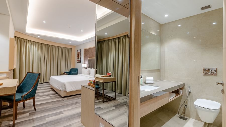 A panoramic image of a suite in ajmer with a bedroom featuring a bed and a writing desk and a stylish bathroomt - Sarovar Portico, Ajmer