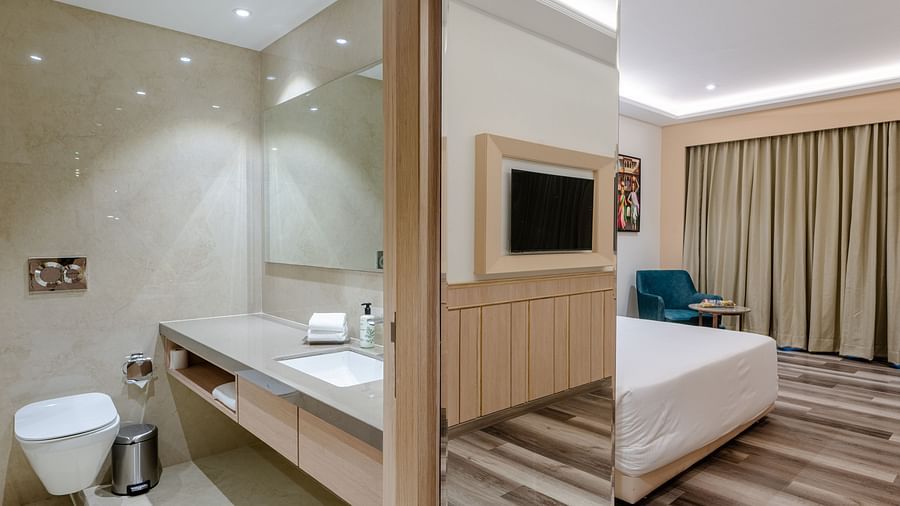 A room with a stylish bathroom with a vanity counter and attached to a bedroom with wooden ascents - Sarovar Portico, Ajmer