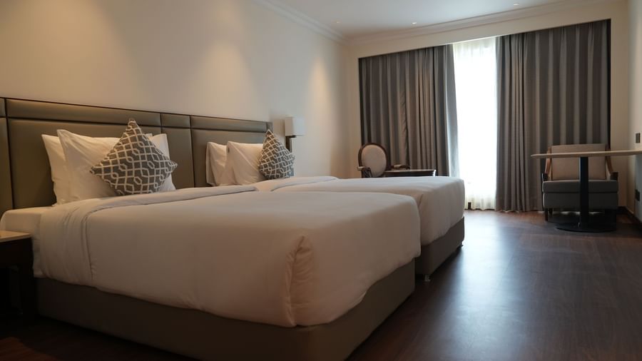 A room with large windows features a seating arrangement with twin beds | Deluxe Twin Bed Room | Sarovar Portico, Hanumangarh