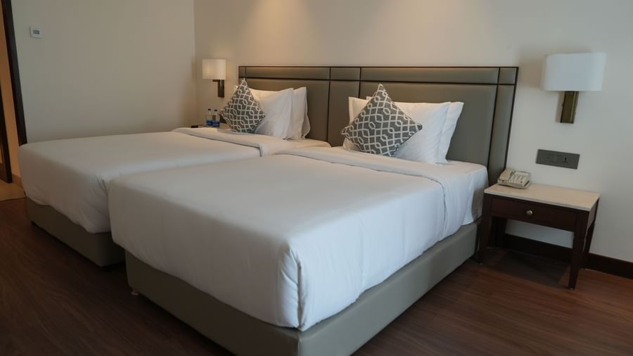 A hotel room featuring two twin beds near bedside tables with lamps | Deluxe Twin Bed Room | Sarovar Portico, Hanumangarh
