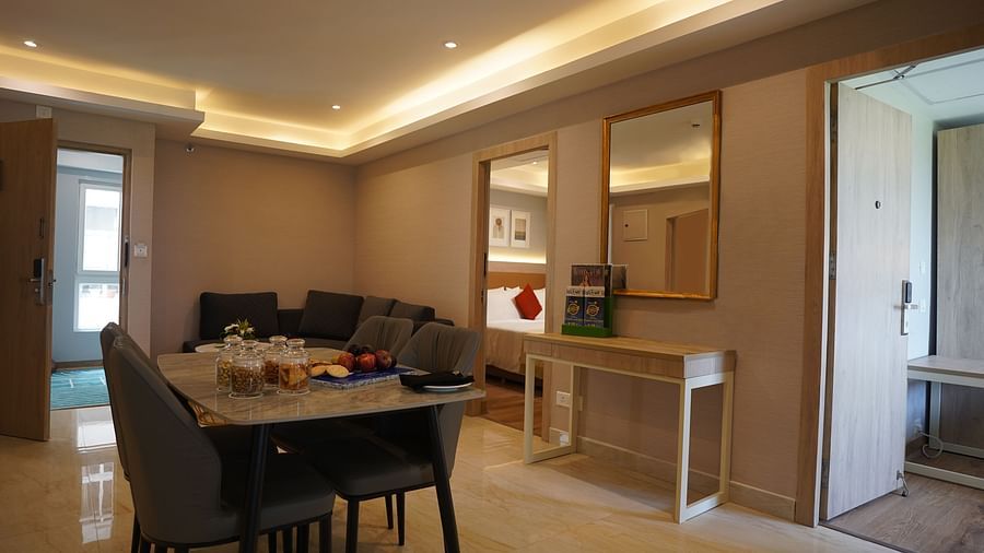 a dining table with chairs, a sectional sofa, and a dressing table with a mirror in the living room of one of the suites at Sarovar Portico, Kolkata Rajarhat