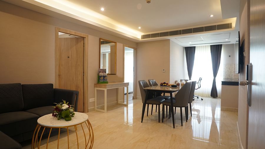 a dining table with chairs, a sectional sofa, and a dressing table with a mirror in the living room of one of the suites at Sarovar Portico, Kolkata Rajarhat