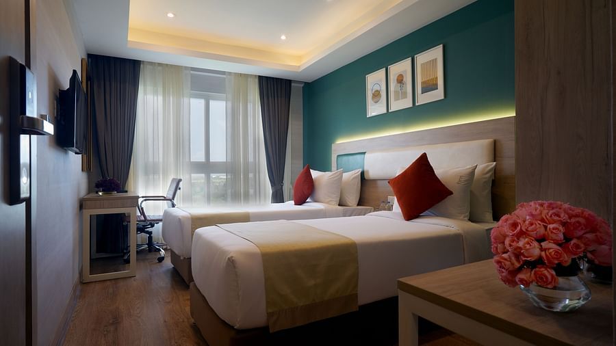 view of twin beds, a side table with a vase, a television, and a work desk and chair inside one of the deluxe rooms at Sarovar Portico, Kolkata Rajarhat