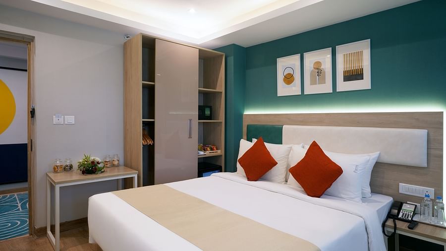 An image of a bed room with a neatly arranged bed, a bed side table, a wardrobe, a study table and modern decor - Sarovar Portico, Kolkata Rajarhat