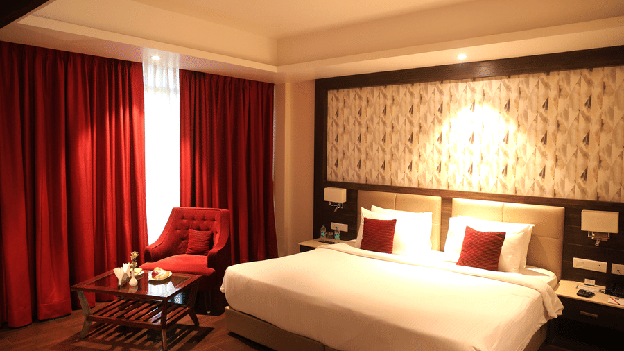 Bedroom at Sarovar Portico, Somnath with a large bed, seating area, patterned wall panel, and curtains.