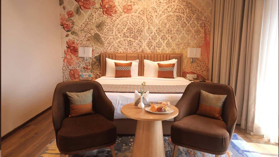 Seating area at Sarovar Portico, Somnath with two chairs, a table with refreshments, and a bed in the background.